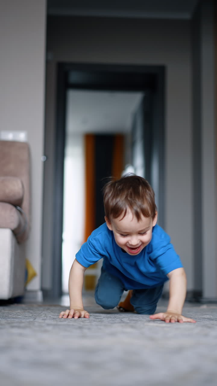 Cheerful energetic Caucasian toddler drops on the floor and crawls approaching the camera. Active time spending at home.