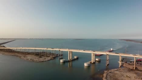 Expansive-aerial-view-of-large-barge-traveling-under-the-JFK-Causeway-at-Corpus-Christi-Bay-along-the-Intercoastal-Waterway-in-Texas