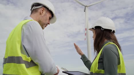 Two-caucasian-engineers-standing-on-wind-turbine-field-and-discussing-over-documents.