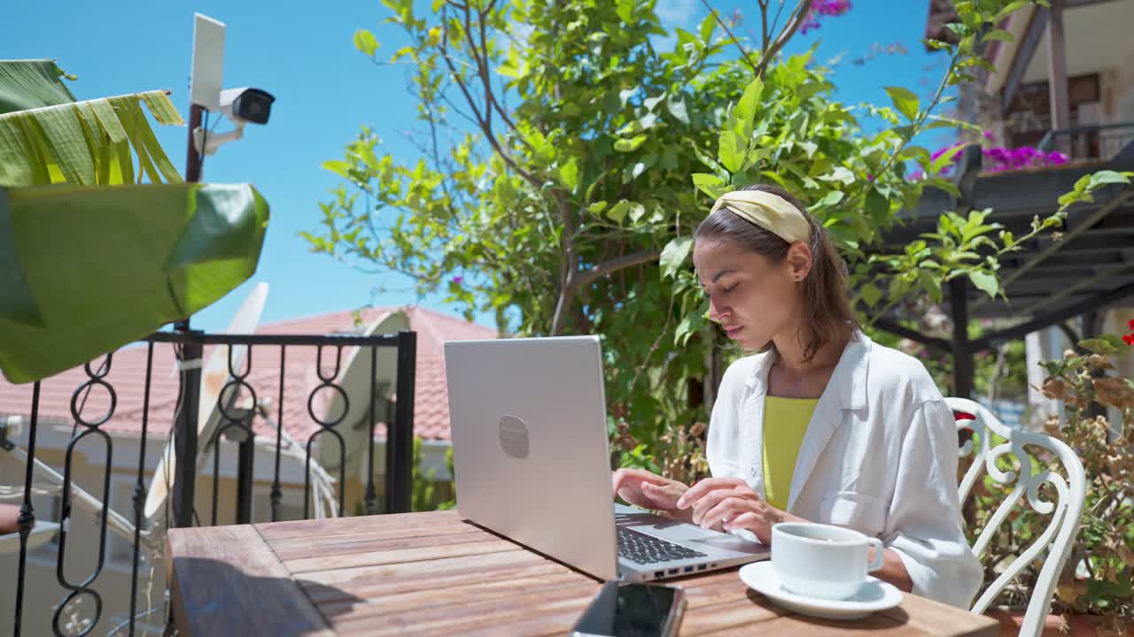 Side view young female businesswoman using laptop outdoors at terrace with palm trees, remote online working during summer vacation