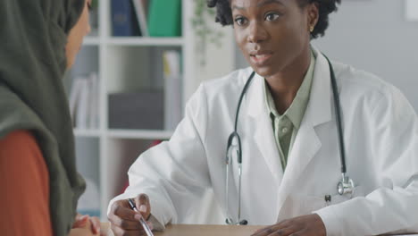 médico o consultor femenino que se reúne con una paciente femenina con pañuelo en la cabeza para discutir las exploraciones