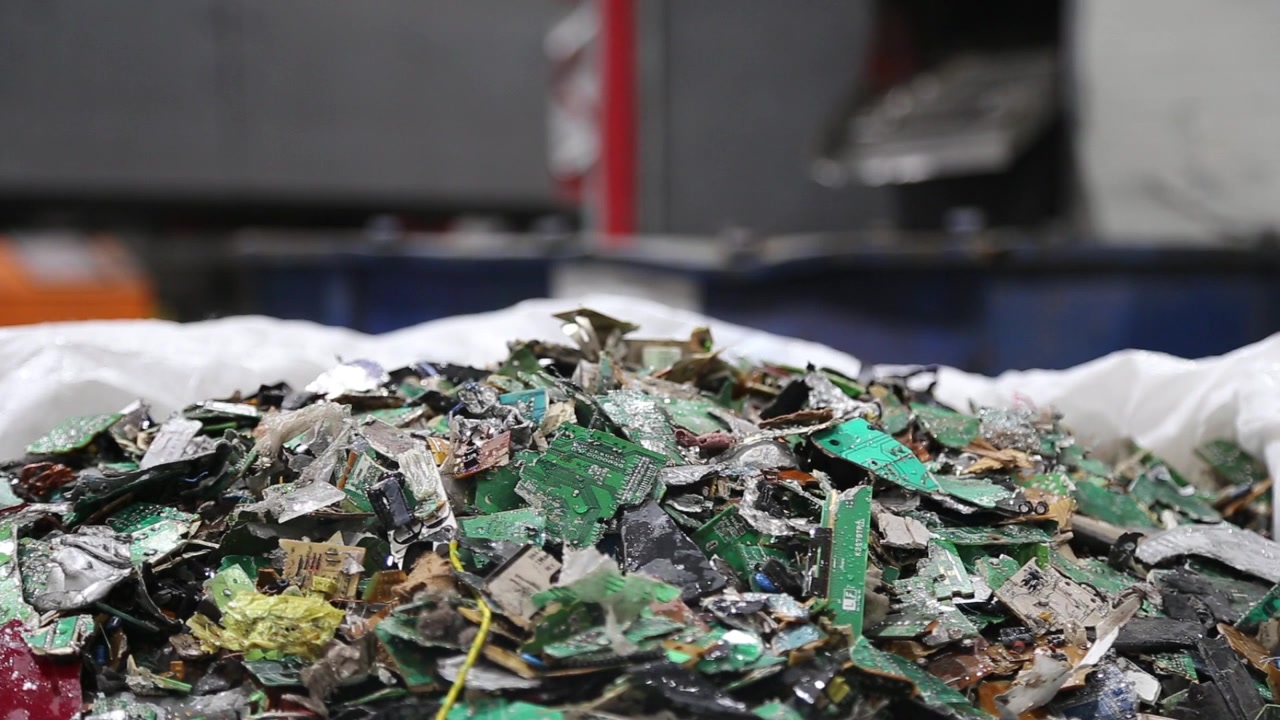 Aerial drone view shows electronic waste and circuit boards piled inside recycling facility. Mixed components highlight e waste recovery and material processing activity indoors.