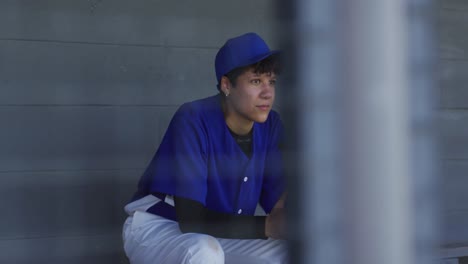 jugadora de béisbol de raza mixta nerviosa, sentada en el banco esperando, sosteniendo una pelota de béisbol