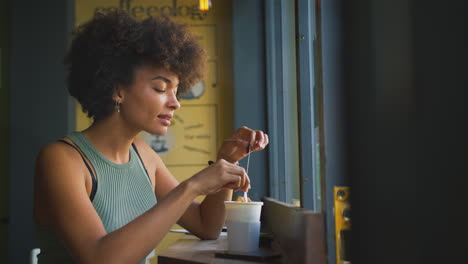 female customer in coffee shop window taking teabag out of cup