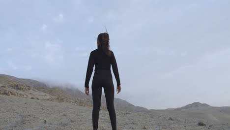 long shot of a woman dressed from the back looking at the desert around her with the cloudy sky