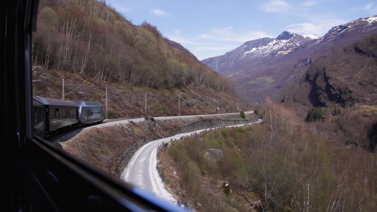 Treno che percorre una curva di montagna con valle panoramica e cime innevate alla luce del giorno primaverile, Norvegia Europa