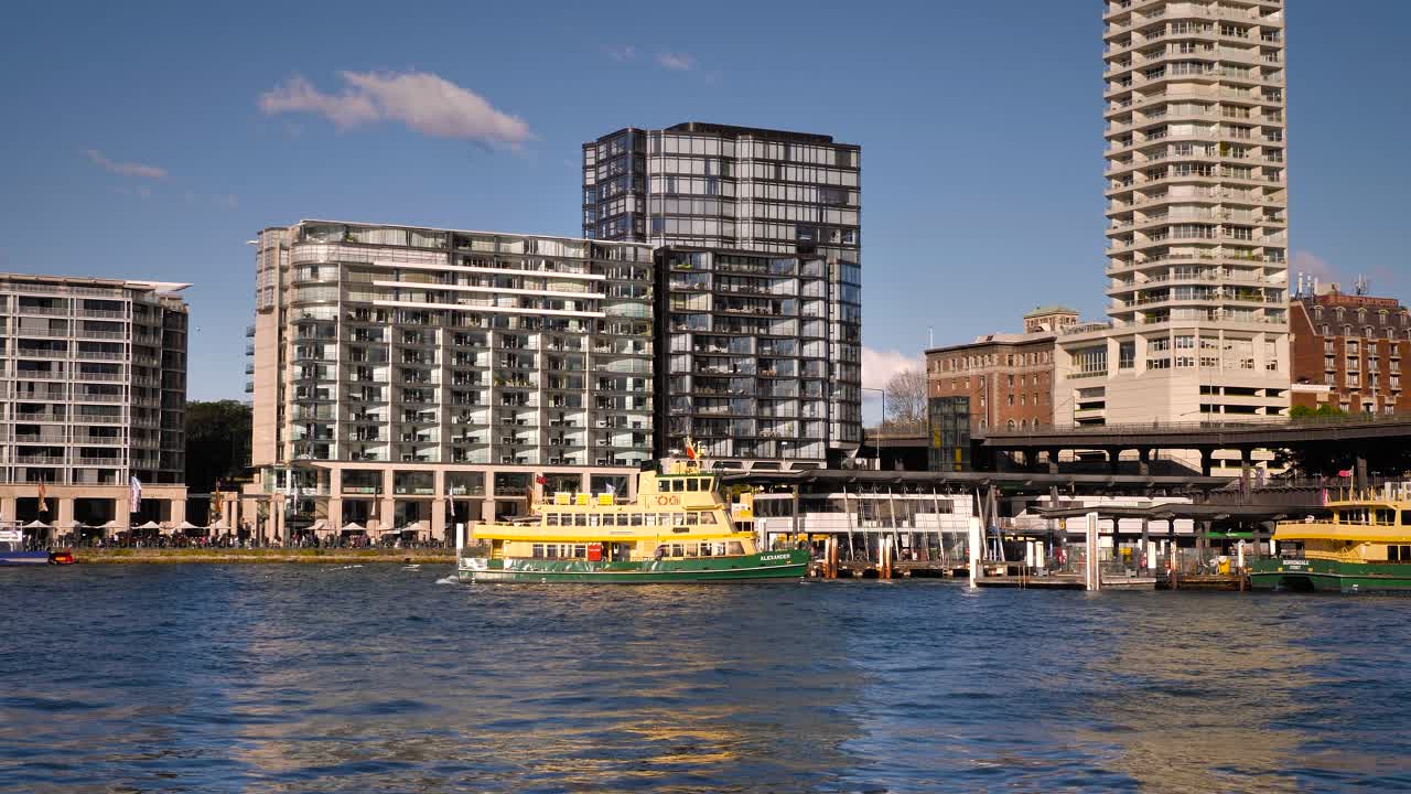 A ferry docked at a bustling urban waterfront with modern high-rise buildings under a clear blue sky