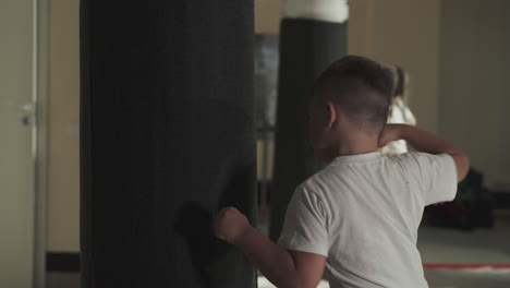 el niño golpea una bolsa colgante enorme en el gimnasio deportivo. el niño pequeño entrena golpeando equipos pesados en la escuela de artes marciales en cámara lenta.