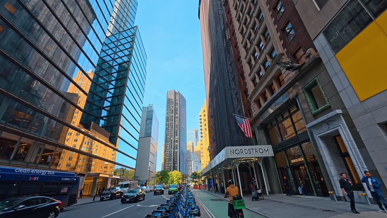 New York, USA, 9 agosto 2025: File di biciclette blu a noleggio presso una stazione stradale cittadina. Stazione di bike sharing blu su una strada di Manhattan con un taxi giallo e un grande magazzino sullo sfondo.
