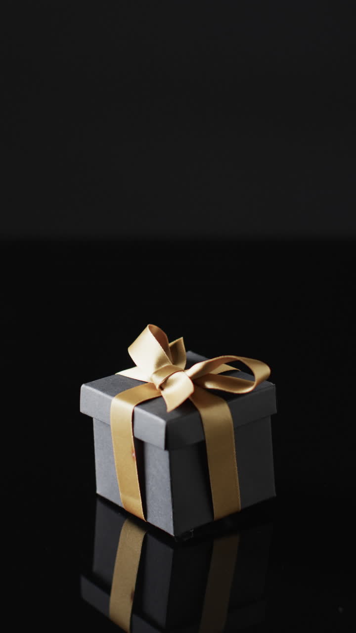 Vertical video of gift box with gold ribbon and copy space over black background