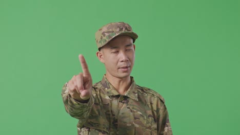 close up of asian man soldier pointing at you and disapproving with no index finger sign while standing in the green screen background studio