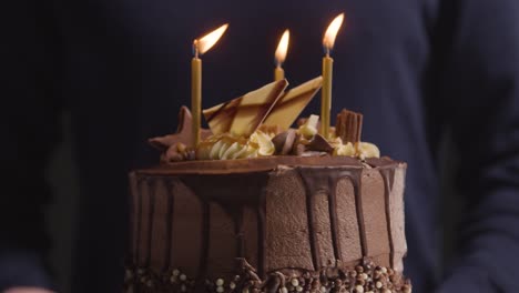 foto de estudio de una persona que sopla velas en un pastel de celebración de cumpleaños de chocolate decorado con fondo negro