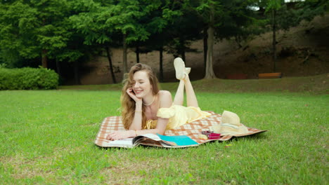 picnic in the park - young ukrainian woman posing while lying on the blanket with book, hat and fruit