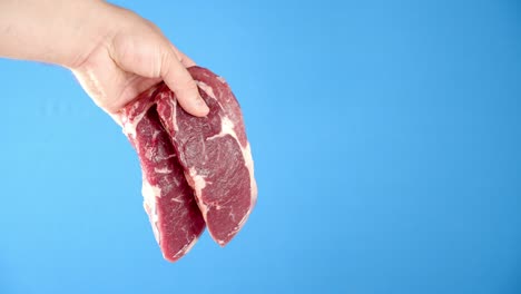 a man's hand holds a steak raw beef ribeye.