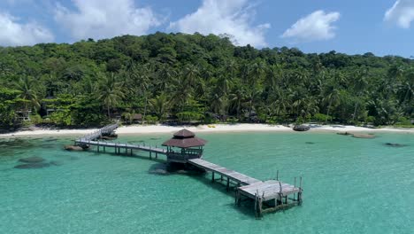 Wide-drone-shot-circling-around-wooden-footbridge-leading-into-the-sea