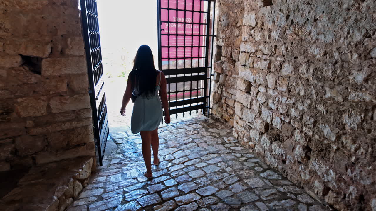 Giovane donna che esce da un'antica porta murata e un sentiero di ciottoli - al rallentatore
