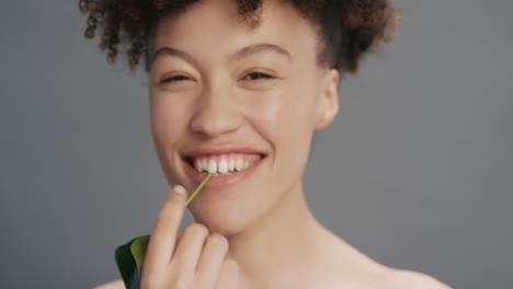 Retrato-Hermosa-Mujer-De-Raza-Mixta-Sonriendo-Acariciando-La-Cara-Con-Hojas-Tocando-Una-Tez-De-Piel-Suave-Y-Saludable-Disfrutando-De-La-Belleza-Natural-Del-Cuidado-De-La-Piel-Sobre-Fondo-Gris