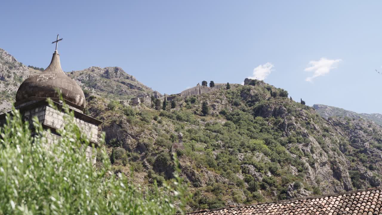 View on the walls leading to the fortress of Kotor from the Kampana Tower also showing the Tower of the orthodox Franciscan Church of Saint Clare and Mountain Landscape of Montenegro in summer time