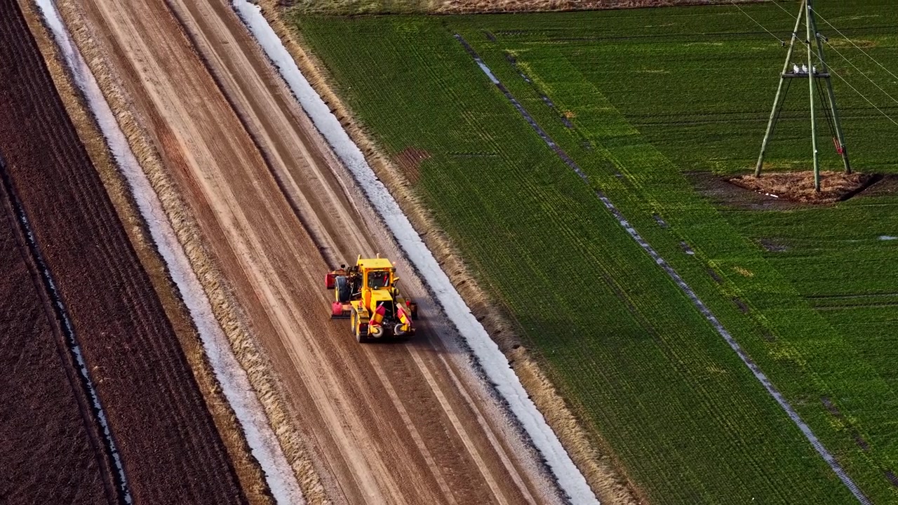 Motolivellatrice che compatta una nuova strada sterrata tra campi agricoli, vista aerea.