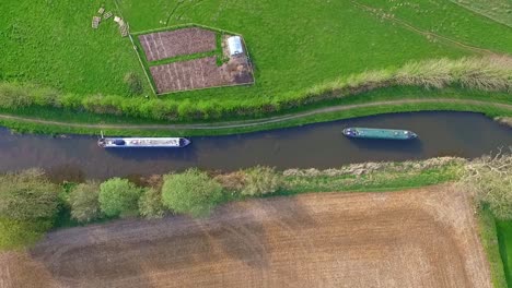 aerial drone shot looking down at canal boat barge slowly making its way along the water in summer