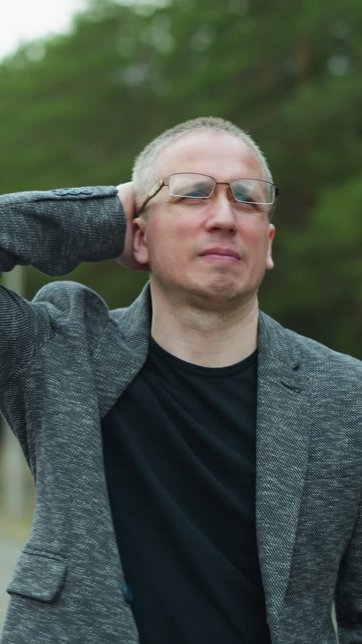 안경과 회색 재을 입은 남자가 철도 트랙에 서서 한 손으로 머리를 문지르고 머리의 뒷부분을 만질 때 괴로워하는 모습