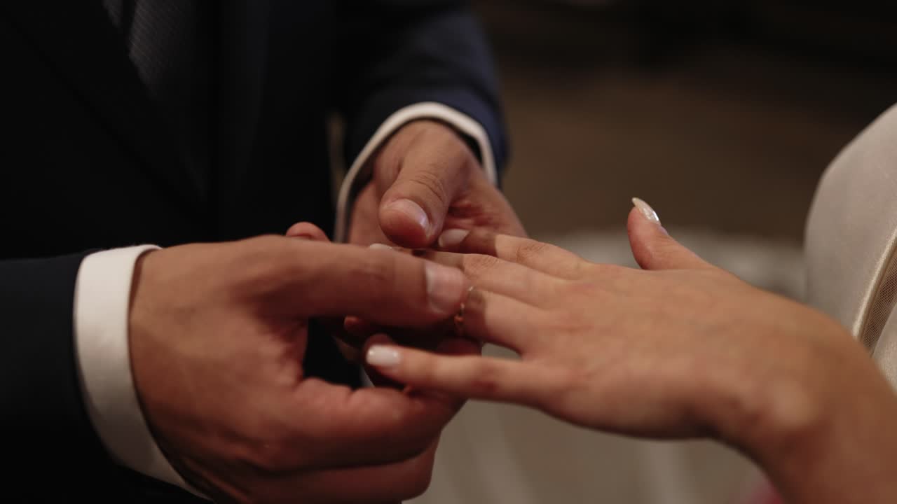 Groom in dark suit gently placing a gold wedding ring on bride's finger during ceremony