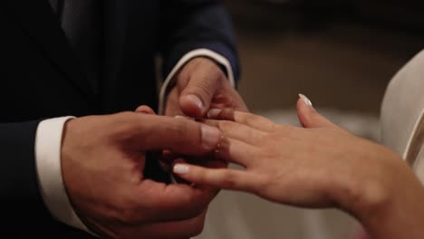 groom in dark suit gently placing a gold wedding ring on bride's finger during ceremony