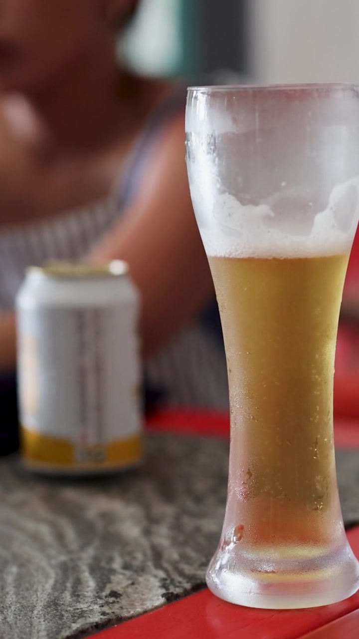 Un alto bicchiere smerigliato di birra chiara è posato su un tavolo con uno sfondo sfocato.