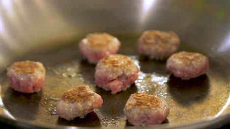 small size juicy meat balls frying in a steel pan, handheld close up shot