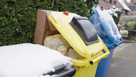 overflowing trash containers covered with snow in city street