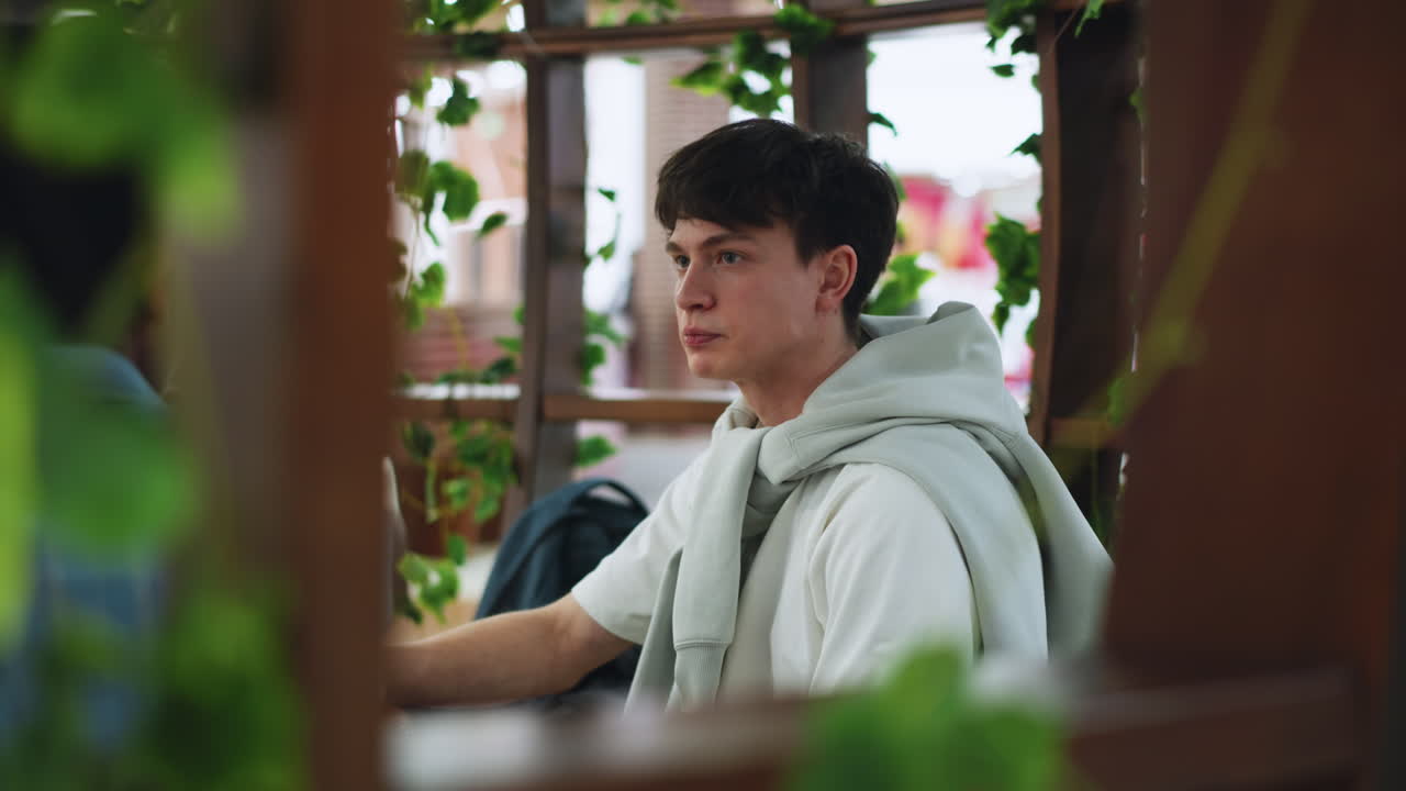 Side view of colleague wearing white sweater listening to friend while chewing food, indoor setting with soft light, facial expression showing attention and engagement during relaxed conversation