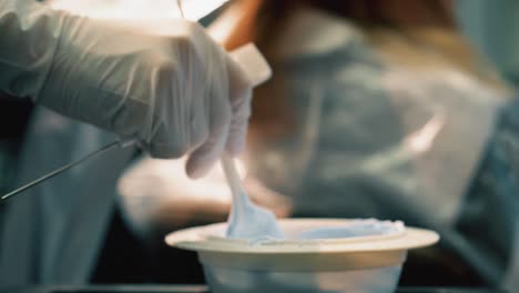 manos con guantes sosteniendo pincel sumerge el tinte de cabello del cuenco luego se mueve para aplicar a la lámina en el cabello del cliente