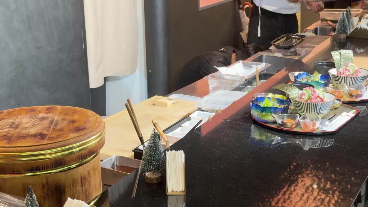 Uno chef di sushi si inchina dietro il bancone dell'omakase con vassoi di sashimi sotto la calda illuminazione del ristorante