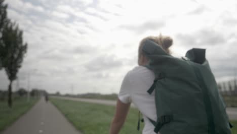 Beautiful-young-blonde-woman-with-backpack-riding-a-bike-on-bike-path-in-Myrte-boerderijen