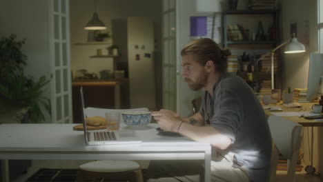 man eating breakfast in front of laptop