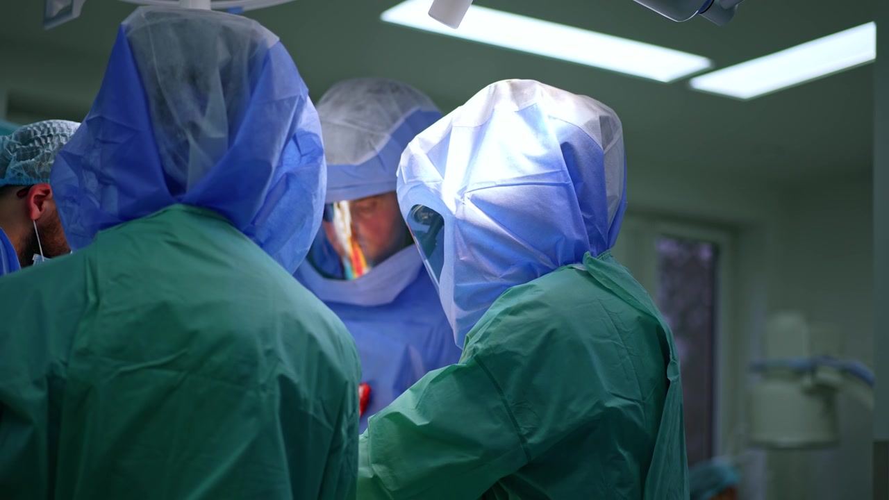 Vista posteriore dei chirurghi con caschi protettivi e uniformi che lavorano al tavolo operatorio. Un team di medici esegue un intervento di chirurgia traumatologica.