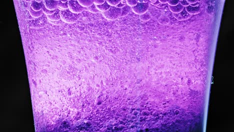 foto macro de un vaso con muchas burbujas violetas flotando y goteando en el agua