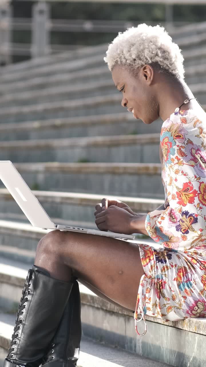 Positive black transgender person typing on laptop on stairs