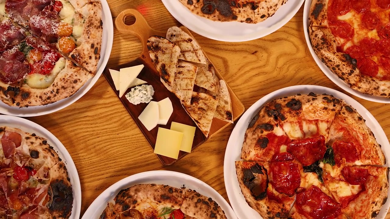 Toma cenital de varias pizzas, pan a la parrilla y tablas de quesos en una mesa de restaurante