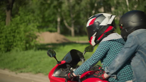 two friends are riding a red power bike with helmets on, traveling along a road with blurred green trees and a metal signpost in the background