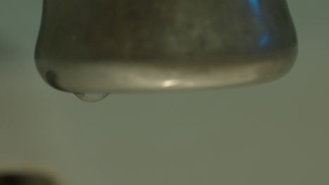 slow motion closeup of a faucet as a single drop of water forms and falls
