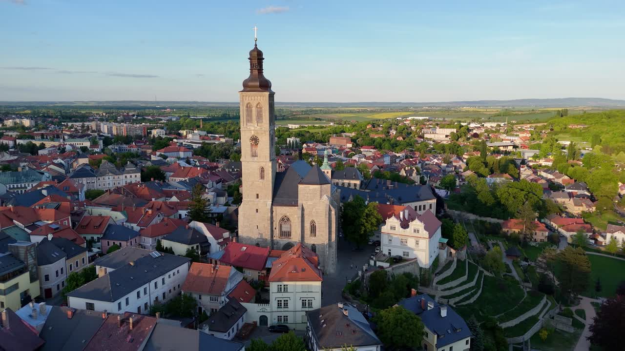 St. James Church tower in Kutna Hora with city streets and red roofs, aerial daytime pass