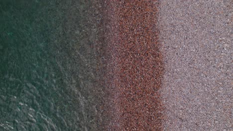 Aerial-top-down-drone-shot-of-the-sea-on-a-sunny-day-on-a-pebble-beach,-Weymouth,-Dorset,-UK