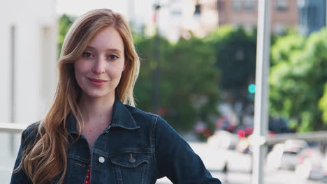 portrait of smiling young businesswoman standing outside office building with city skyline behind