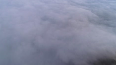 a 4k drone shot above low-lying clouds, flooding over mountain tops and down into a valley, near david m