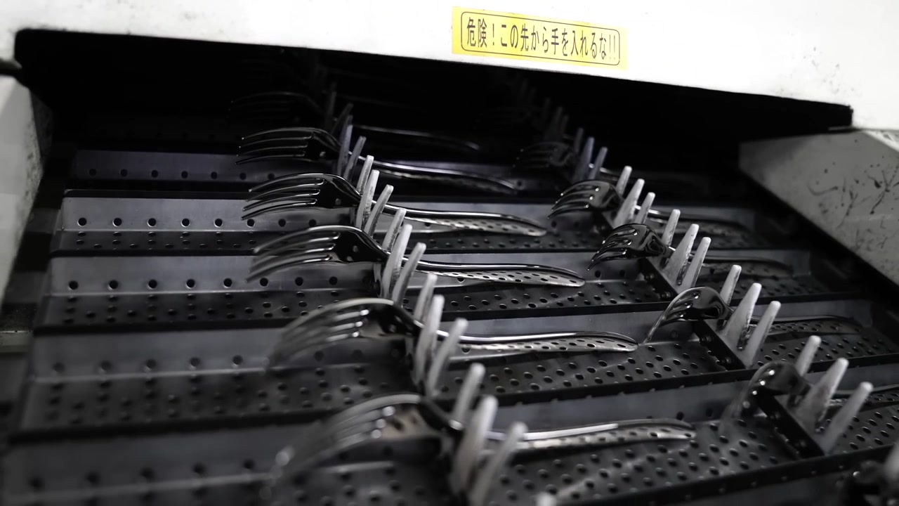 Polished forks held by fixtures traveling through automated buffing machine with Japanese warning sign