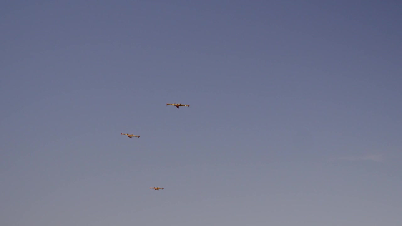 Tre brandslukningsfly nærmer sig sammen over en klar blå sommerhimmel.