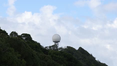 la cúpula del radar gira lentamente en la cima de una montaña verde y exuberante.