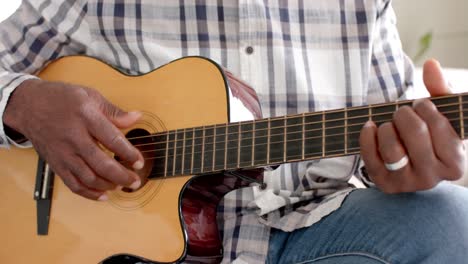 Hombre-Mayor-Afroamericano-Enfocado-Tocando-La-Guitarra-En-Casa,-Cámara-Lenta