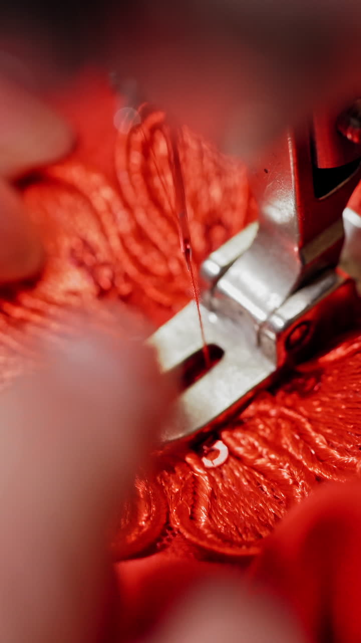 Sewing process on red fabric making a design with a beautiful flower. Hands of seamstress are holding material while working on sewing machine. Close-up. Vertical video